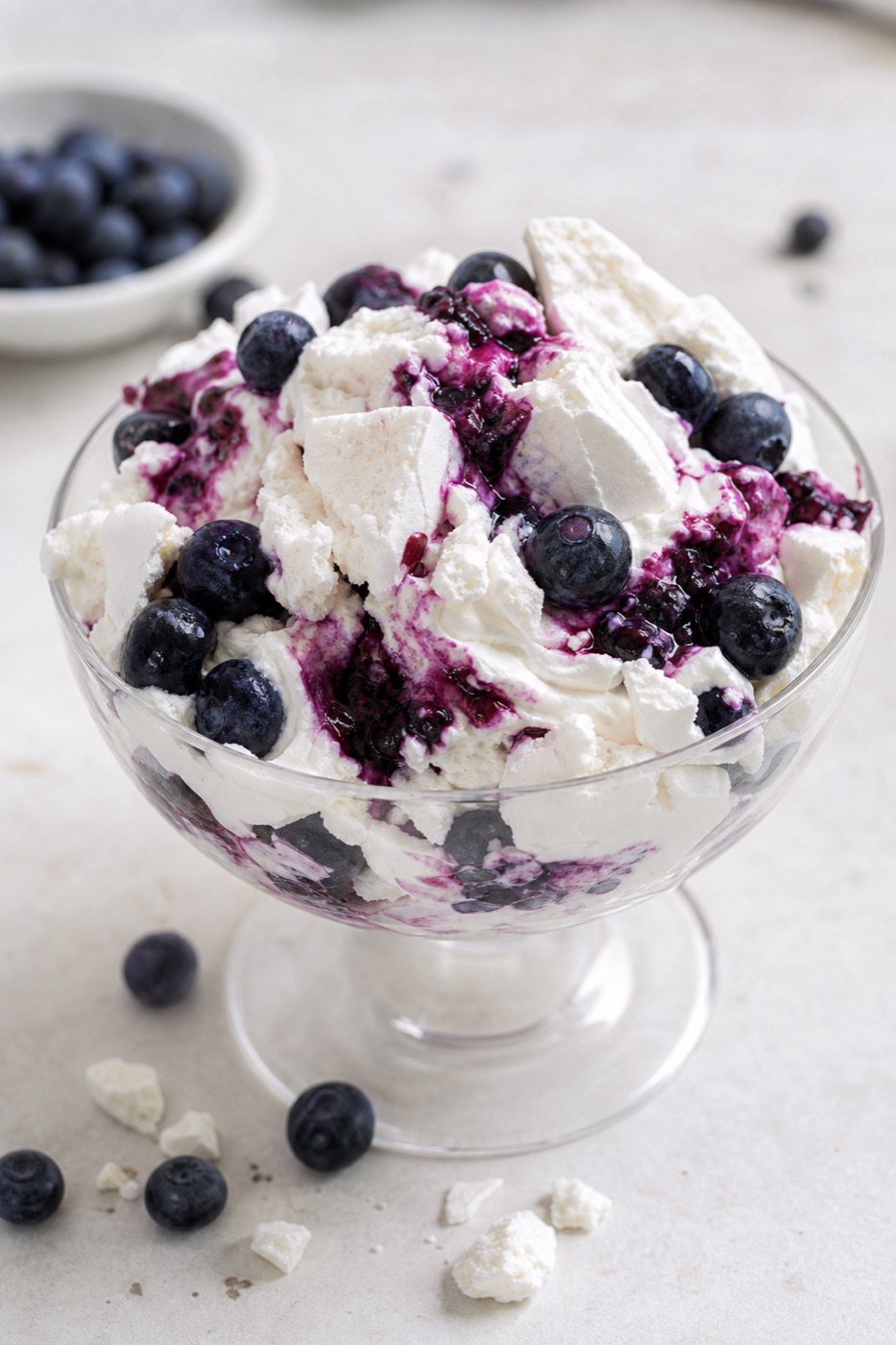A glass dish of Eton mess with crumbled meringue, whipped cream and blueberries